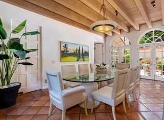 The dining room has vintage chairs and a large oval glass table. The roof has exposed beams and the floor tiles are terracotta