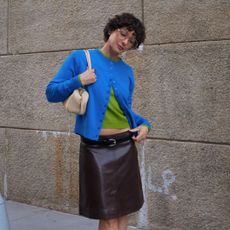 a woman wearing a blue cardigan, green t-shirt, brown leather skirt, and a tan shoulder bag