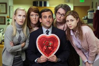 the cast of the office surround steve carrell as he holds a red heart valentine