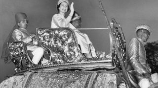 Britain's Queen Elizabeth II waves to the crowd as she rides an elephant next to Maharaja of Jaipur Man Singh II at the City Palace in Jaipur on January 24, 1961. (Photo by CENTRAL PRESS / AFP)