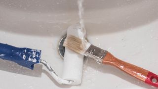 A paint brush and roller under running water in the sink
