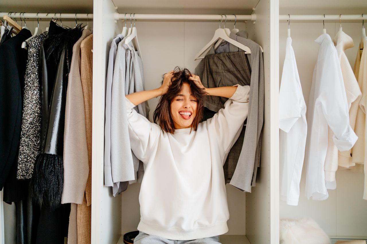 A woman is celebrating her capsule wardrobe. She stands between the clothes that are hanging in a closet.