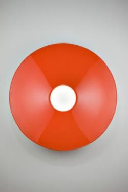 Left: A man looking at a large red circle on the wall with a hole just off of centre. Right: A man leaning back against a wall inbetween two flag-like objects attached to the wall. 