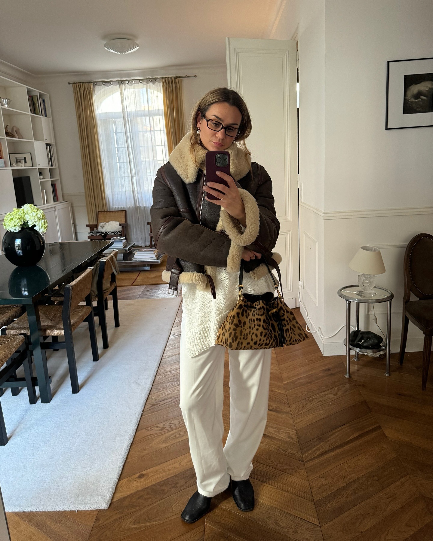 Woman in a shearling coat, white pants, and a leopard print bag