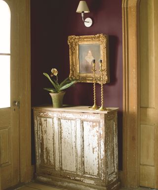 Burgundy hallway idea by Benjamin Moore with white distressed wooden cabinet and framed wall art