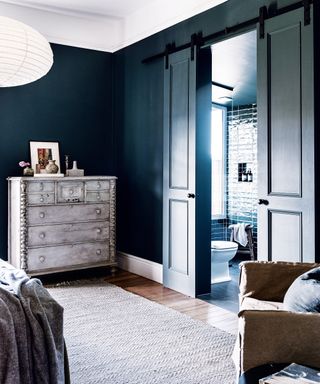 bedroom with dark blue walls, limewashed chest of drawers and neutral rug