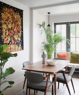 A dining room with white panelled walls, floor to ceiling windows and greenery
