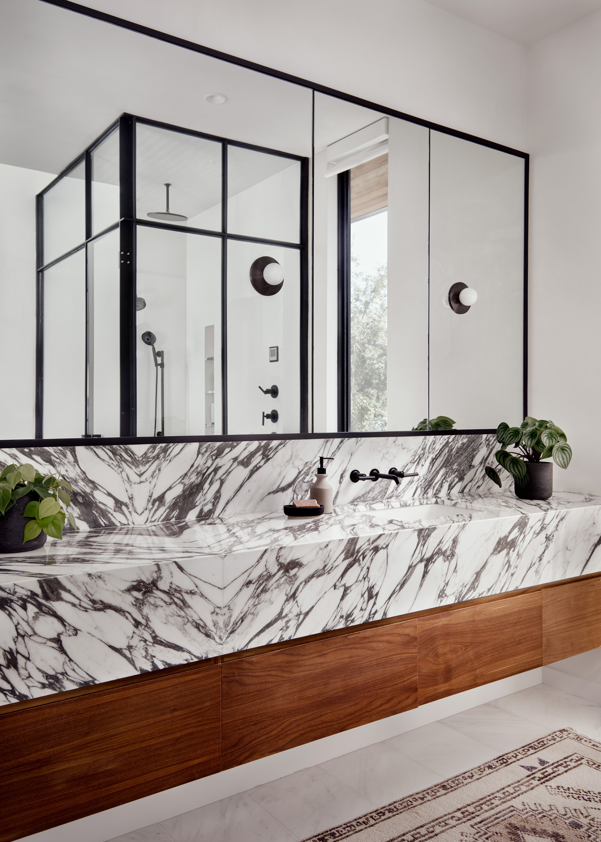 A white bathroom with mirrored cabinets, marbled counters, and a pair of potted plants