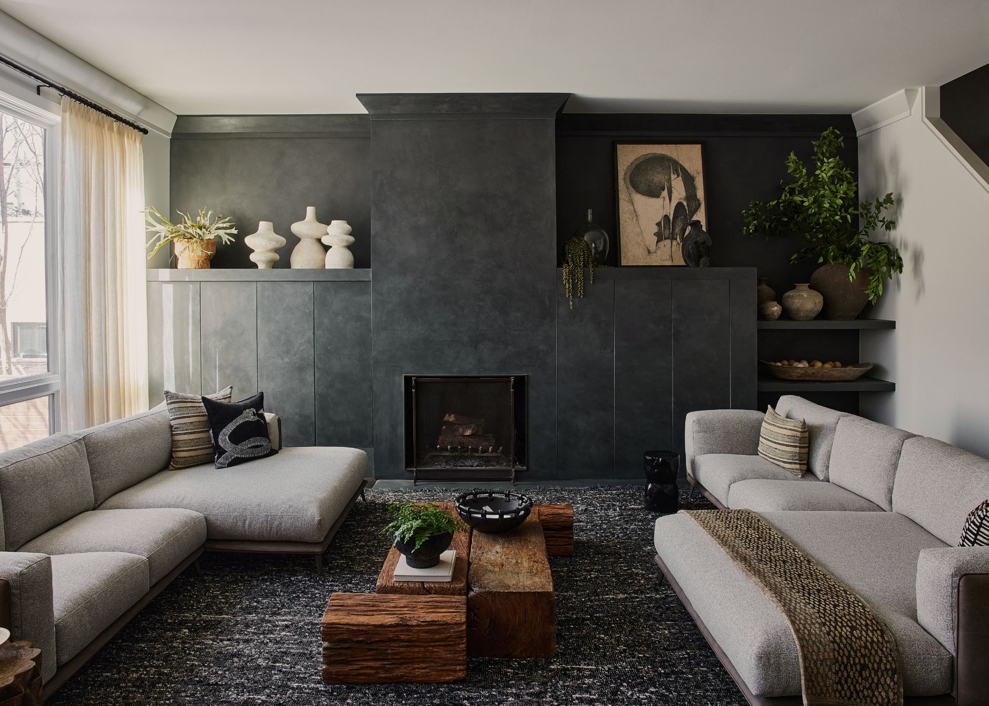 A living room with dark carpet, dark walls, a fireplace and cream toned sofas