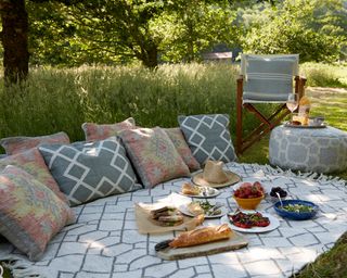 Garden decorating ideas showing a rug laid out on grass with cushions and picnic food