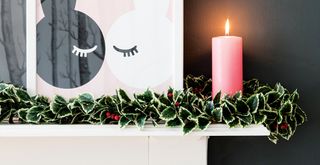 Dark grey living room with a white mantel piece with a holly leaf garland and a pink lit candle