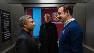 (L to R) Mohammed as Nathan "Nate" Shelley and Jason Sudeikis as Ted Lasso stare at each other in an elevator while Anthony Head as Rupert Mannion looks on from outside the elevator in the first photo released from Ted Lasso season 3.