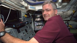 marc garneau looking over his shoulder near control panels in the space shuttle