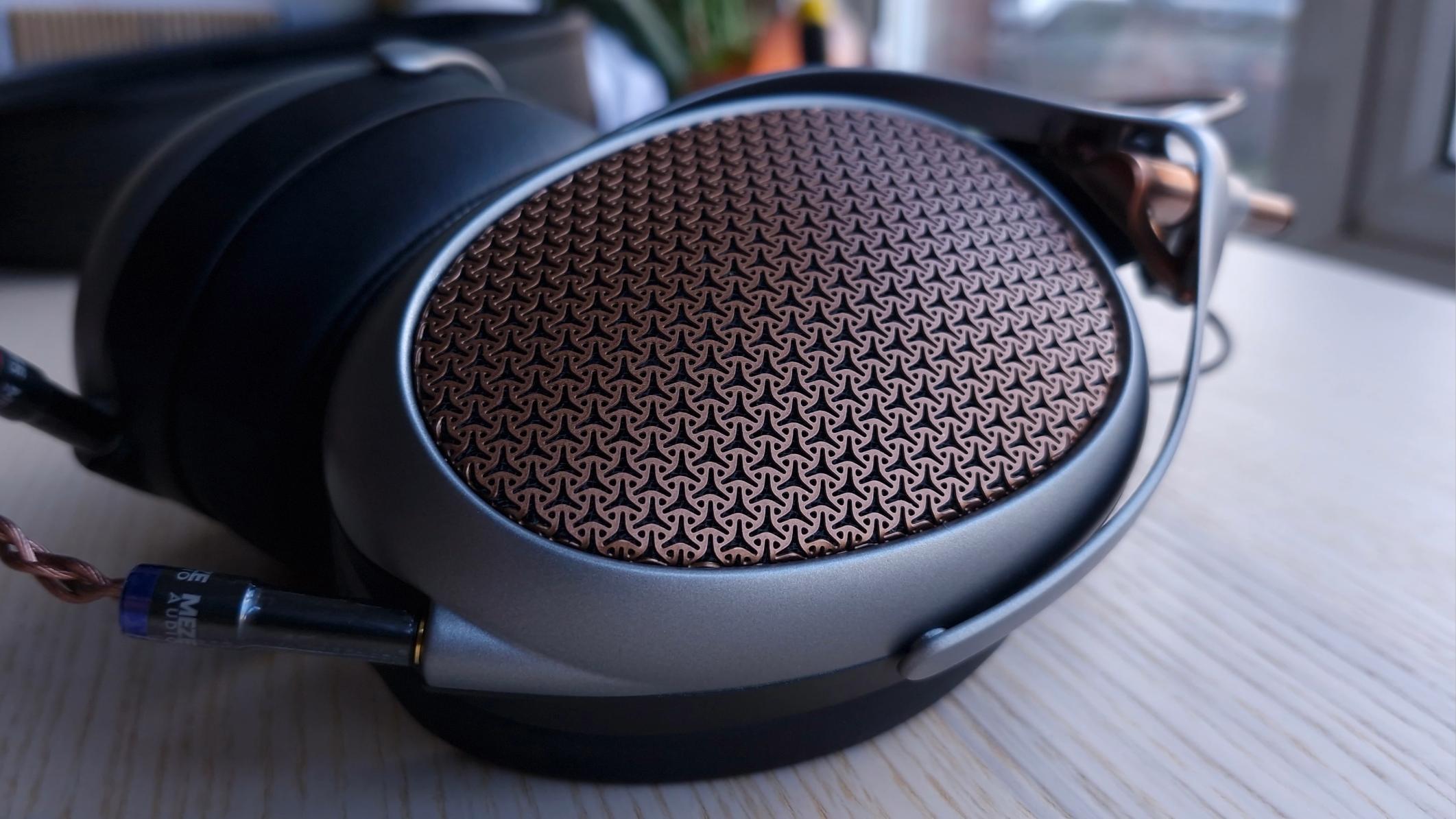 Earcups of the Meze Audio Poet open-back over-ear headphones, on a wooden surface