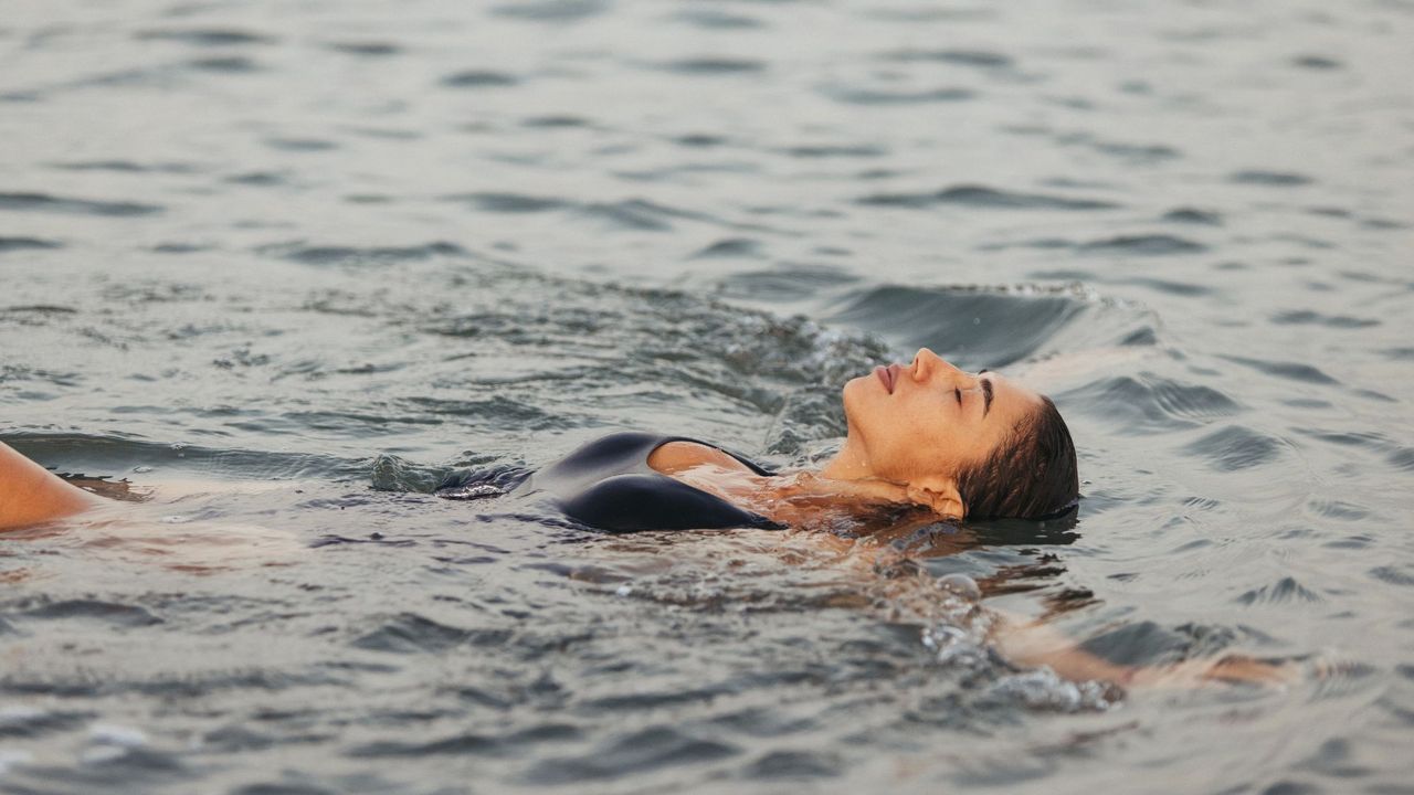 An image of a woman floating on her back in the sea, resembling the smell of Ouai St Barts Hair &amp; Body Mist