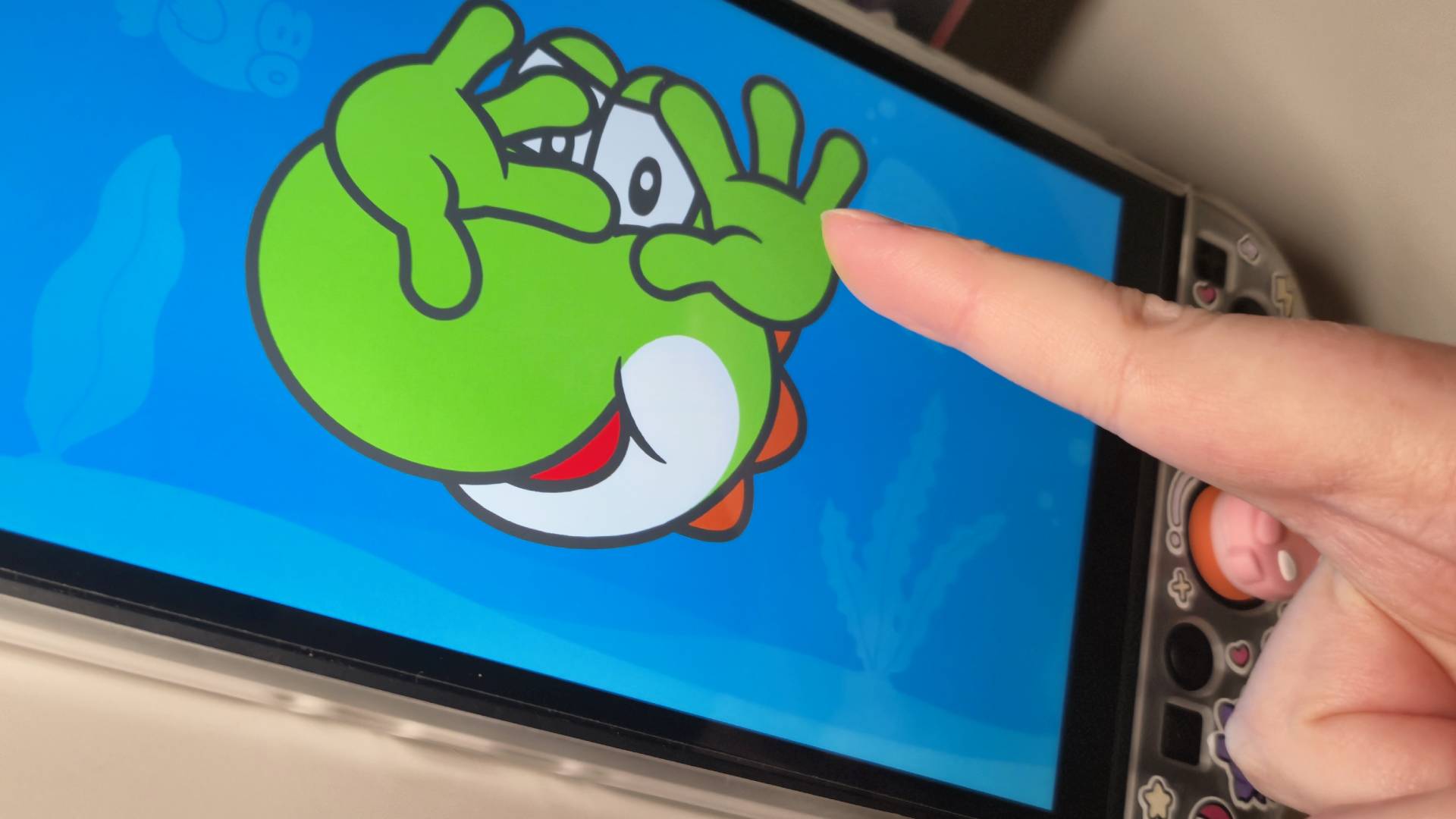Photo of a human finger pointing towards Hello, Yoshi! running on a Switch 2 screen.