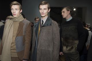 Three models stood with two wearing brown jackets and one wearing a jumper