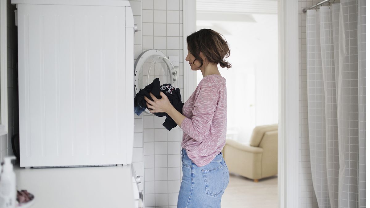 Woman wearing a pink top loading laundry into a front load tumble dryer.