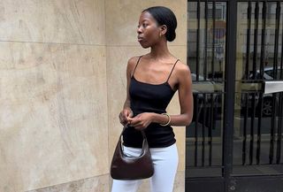 Sylvie Mus wearing a black camisole and white capri pants with a brown bag.