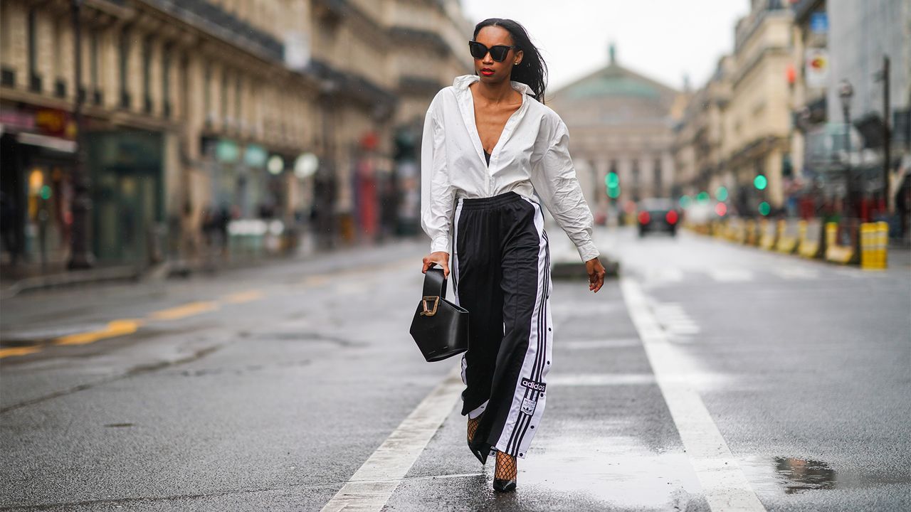 PARIS, FRANCE - JANUARY 23: Emilie Joseph wears sunglasses, a white oversized long shirt from &amp; Other Stories, black bras from Aubade, a Danse Lente black leather bag, black and white striped Adidas flared jogger sport pants, fishnet tights from Calzedonia, black high heeled pointy shiny shoes from Cosmo Paris, on January 23, 2021 in Paris, France. (Photo by Edward Berthelot/Getty Images)