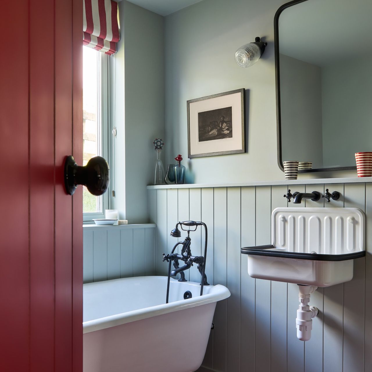 A bathroom with red doors and a bathtub painted in Farrow &amp; Ball's light blue