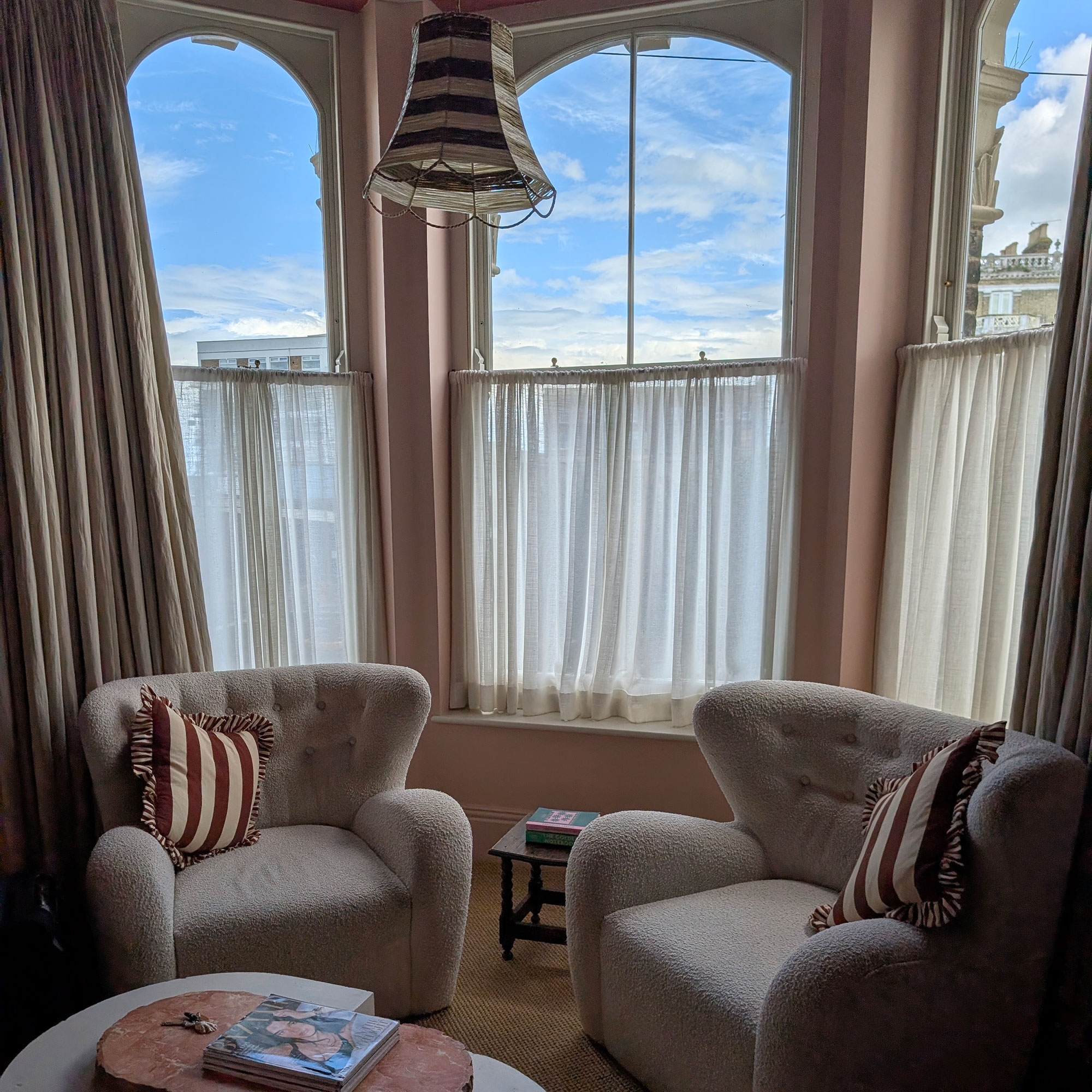 Two cream boucle armchairs sitting in bay window area with semi-sheer cafe curtains