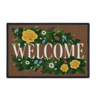 A dark brown welcome mat that says 'welcome' in white lettering with green shrubbery with yellow roses and small blue and white flowers on the top and bottom of the letters