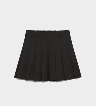 a black pleated aritzia skirt in front of a plain backdrop