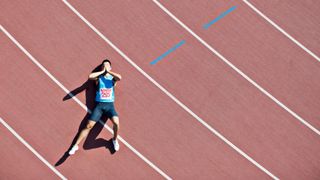 Exhausted and frustrated male runner lying on a red running track covering his face with his hands.