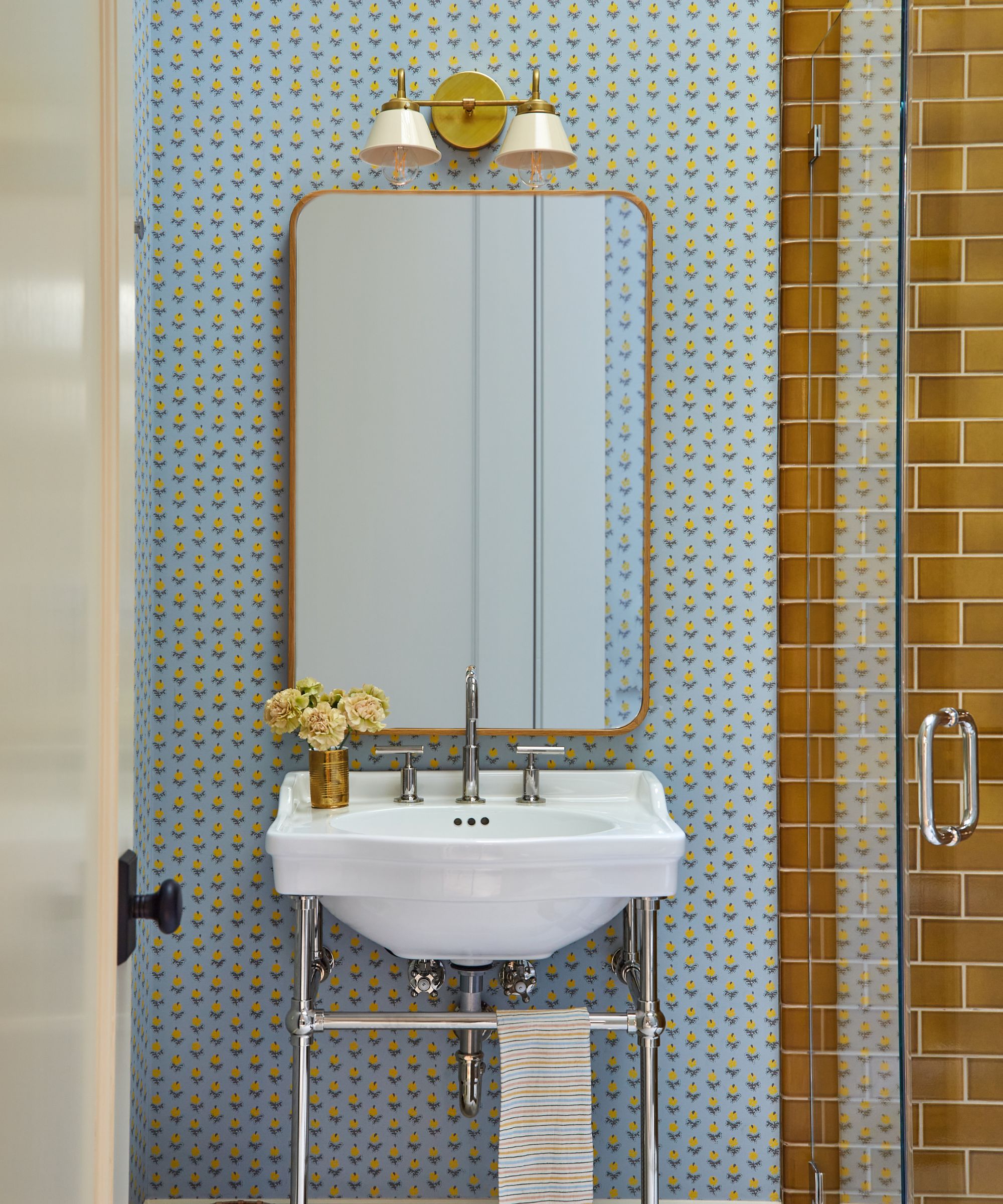 A small bathroom with powder blue wallpaper and ochre tiles in the shower.