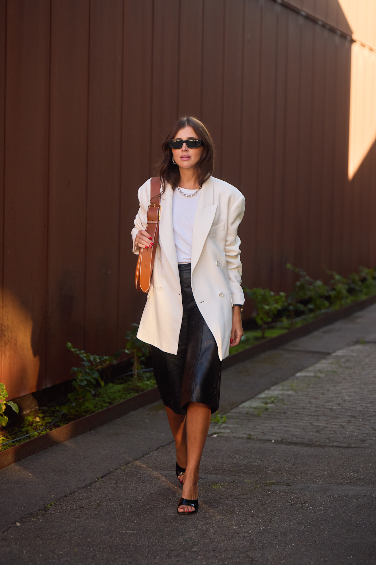fashion week attendee wears white blazer, leather shorts, black sandals
