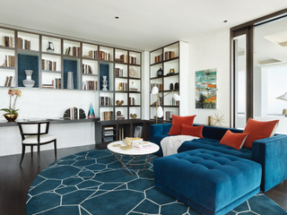 A living room with teal sofa and rug, and bright red pillows