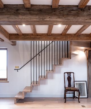 wooden beamed ceiling in hallway with cantilevered stairs, thin black balustrades and chair