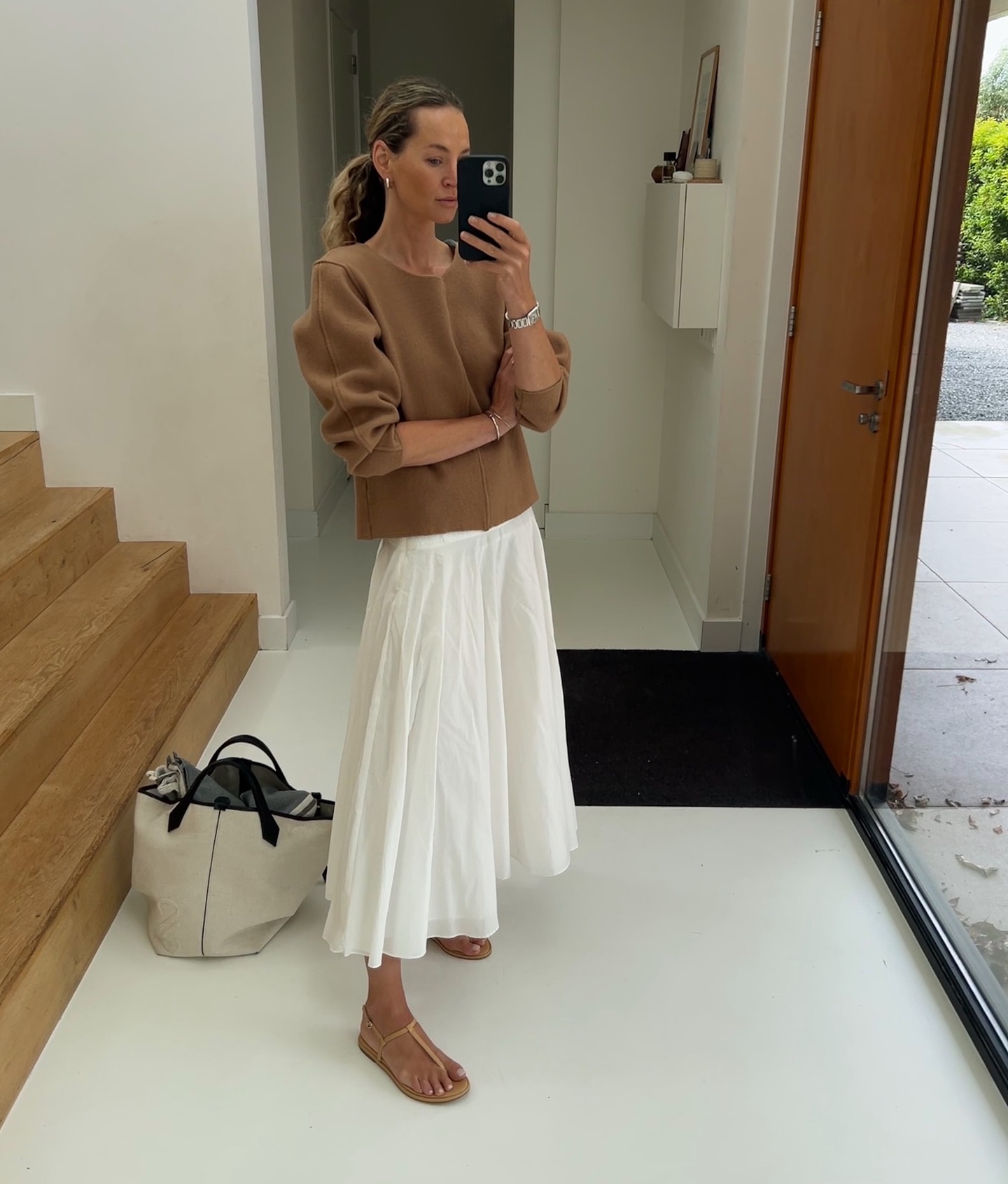 Woman wears brown top, white skirt, t-bar sandals and canvas tote bag