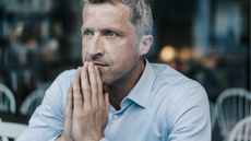 A man looks worried as he clasps his hands in front of his chin.