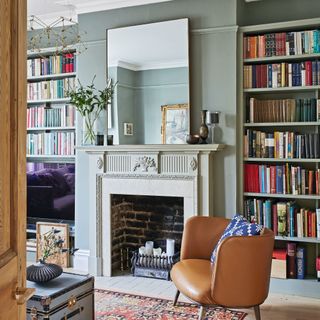 grey green living room with built in bookcase, fireplace with large mirror on top