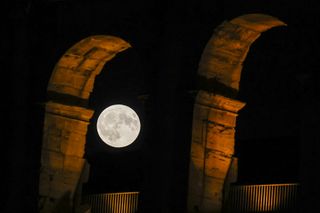 A large moon between the arches of the Colosseum