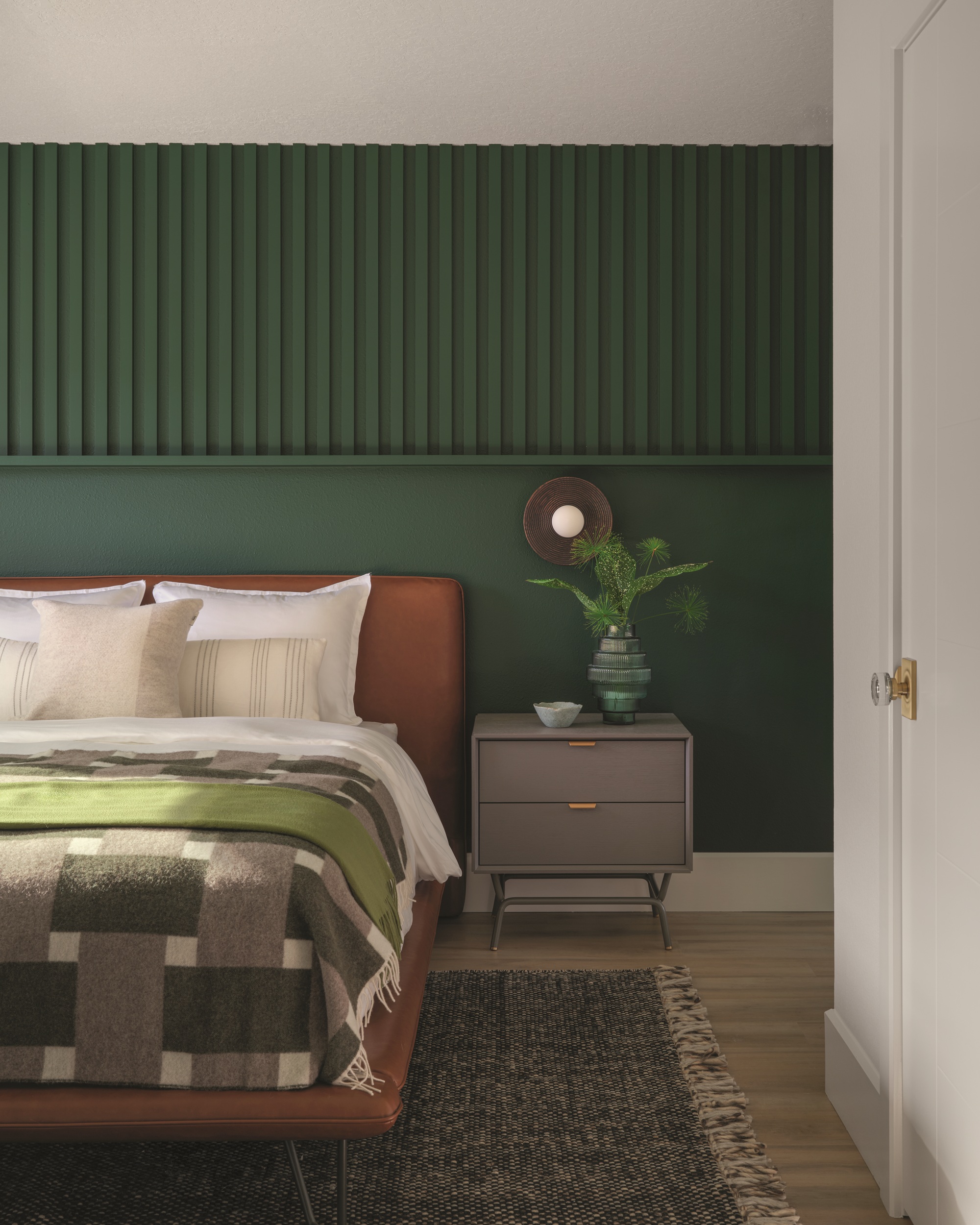 a dark green bedroom with fluted wall paneling and a brown leather bed