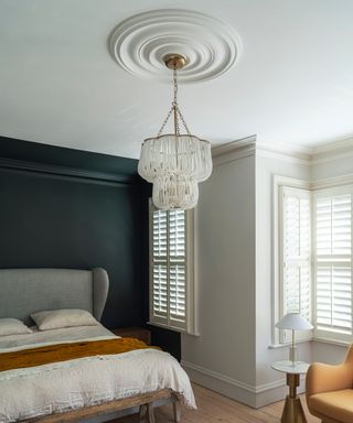 bedroom with dark green wall, white shutters and white ceiling showcasing rose and modern chandelier