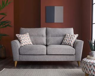 A grey sofa with wooden feet in a living room with a burgundy wall
