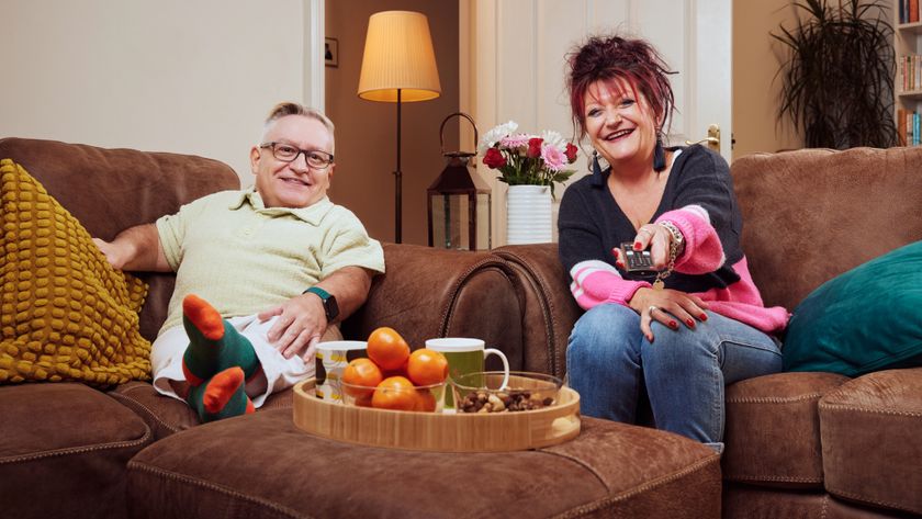 Simon and Jane sitting on a brown sofa and smiling to the camera 