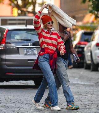 A photo of Gigi Hadid wearing two striped sweaters and a cream-colored crewneck with jeans