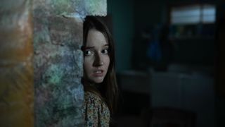 Kaitlyn Dever peers round a round a brick wall in No One Will Save You
