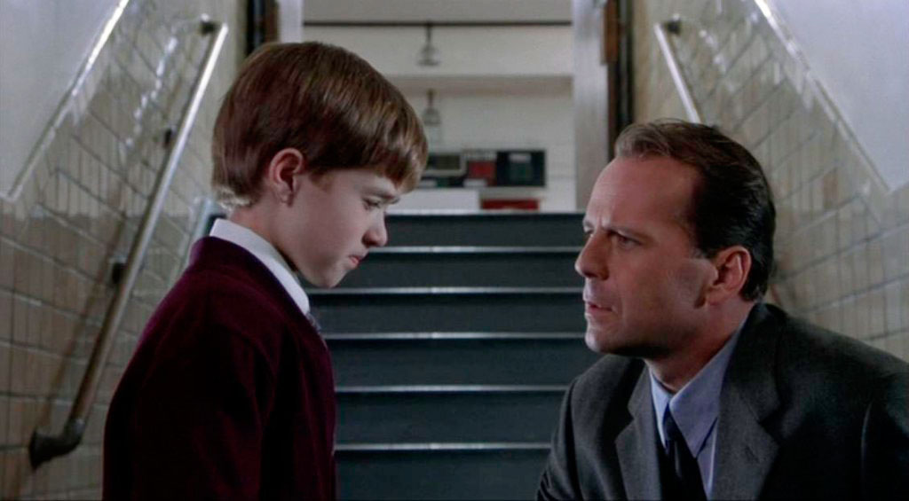 A still from the movie The Sixth Sense showing characters Malcolm (played by Bruce Willis) and Cole (played by Haley Joel Osment) talking at the bottom of a flight of stairs.