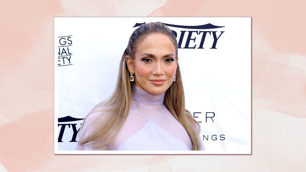 Image of Jennifer Lopez smiling with brunette half-up half-down hair and wearing a lilac dress, on a pink watercolour background