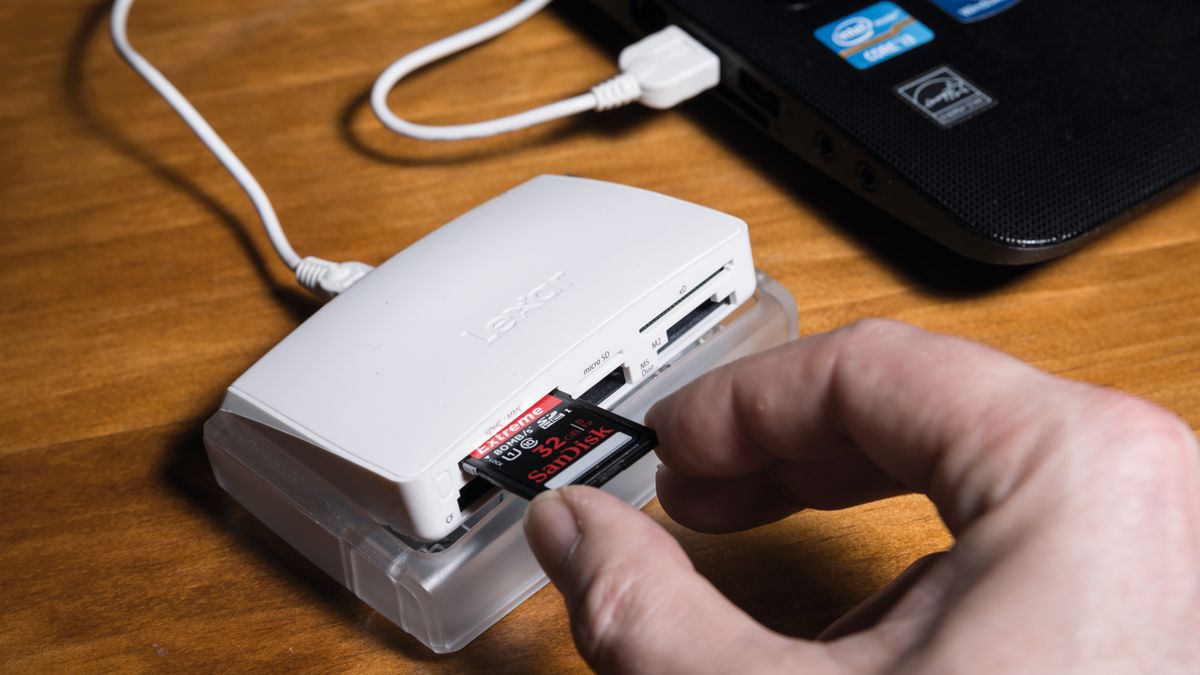 Hand putting SD card into a card reader attached to a laptop on a desk