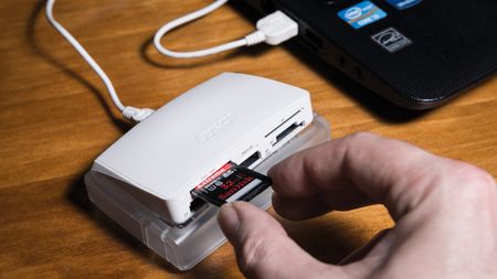 Hand putting SD card into a card reader attached to a laptop on a desk