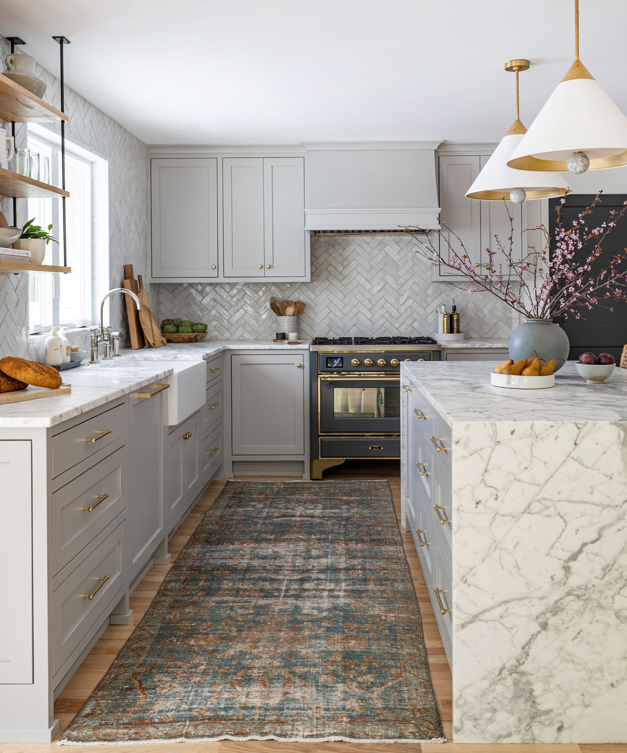 A kitchen with light gray cabinets, a marble island and countertop, a black and gold range cooker, and a vintage rug