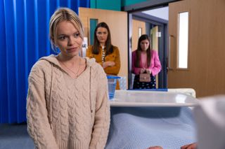 Dilly by Jeremy's hospital bed as Sienna and Maxine look on.