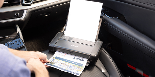 A canon printer in the front passenger seat of a car prints a document.